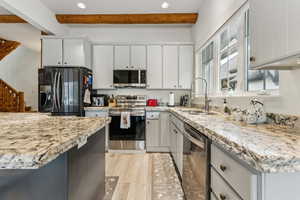 Kitchen with beamed ceiling, white cabinets, a sink, and stainless steel appliances