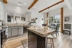 Kitchen featuring light wood-type flooring, stainless steel appliances, a center island, beam ceiling, and visible vents