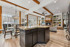 Kitchen featuring open floor plan, a stone fireplace, ceiling fan with notable chandelier, and light wood-style floors