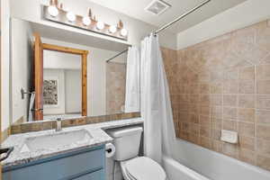 Bathroom featuring toilet, vanity, shower / tub combo, and visible vents