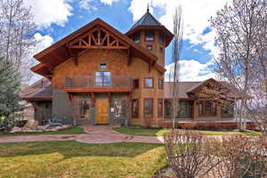 Rear view of house featuring a balcony, a lawn, and stucco siding