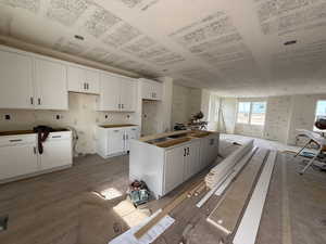 Kitchen with white cabinets, light wood finished floors, a sink, open floor plan, and a center island