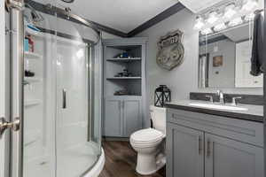 Bathroom with vanity, crown molding, toilet, a stall shower, and wood finished floors