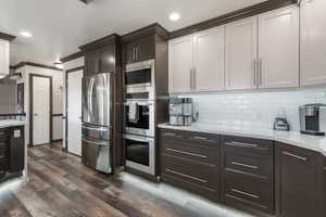 Kitchen with dark wood-style flooring, light stone countertops, stainless steel appliances, and tasteful backsplash