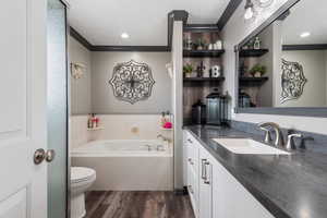 Bathroom featuring vanity, crown molding, toilet, a garden tub, and wood finished floors