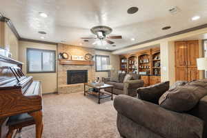 Living area featuring carpet flooring, ornamental molding, a textured ceiling, ceiling fan, and a fireplace