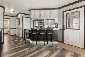 Kitchen with stainless steel refrigerator with ice dispenser, ornamental molding, a breakfast bar, dark wood finished floors, and a peninsula