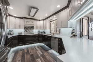 Kitchen featuring dark wood-style flooring, stainless steel appliances, backsplash, a sink, and dark cabinets
