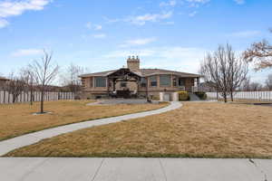 View of front of house with a patio area, a chimney, an attached garage, fence, and a front lawn