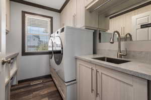 Clothes washing area featuring washer and clothes dryer, a sink, dark wood-type flooring, cabinet space, and ornamental molding