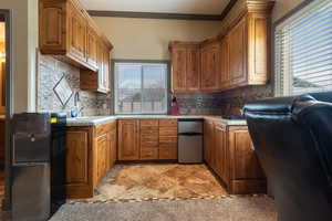 Kitchen featuring light countertops, ornamental molding, fridge, and brown cabinets