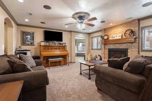 Carpeted living room featuring arched walkways, visible vents, a brick fireplace, and plenty of natural light