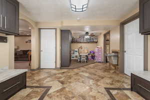 Kitchen with light countertops, a ceiling fan, dark brown cabinetry, and arched walkways
