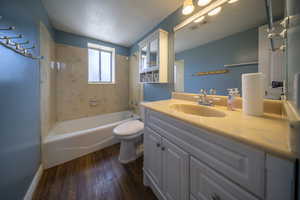Bathroom with visible vents, vanity, wood finished floors, toilet, and bathtub / shower combination