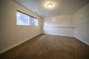 Carpeted empty room with a textured ceiling, visible vents, and baseboards