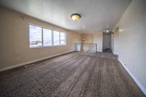 Carpeted empty room with visible vents, a textured ceiling, and baseboards