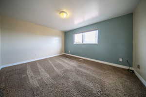 Empty room featuring carpet flooring, a textured ceiling, baseboards, and visible vents