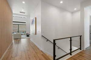 Corridor with wood finished floors, visible vents, baseboards, recessed lighting, and an upstairs landing