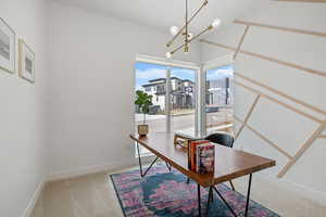 Office area featuring baseboards, light carpet, and a notable chandelier
