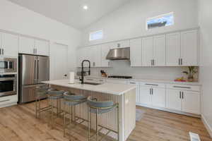 Kitchen with high vaulted ceiling, under cabinet range hood, a sink, stainless steel appliances, and a breakfast bar area