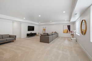 Carpeted living area featuring a raised ceiling, recessed lighting, and visible vents