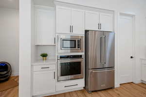 Kitchen featuring white cabinetry, stainless steel appliances, light countertops, and light wood-style floors