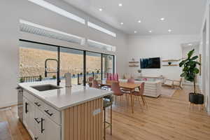 Kitchen with light wood-type flooring, a high ceiling, a sink, stainless steel dishwasher, and open floor plan