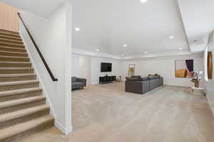 Carpeted living area with a raised ceiling, stairway, recessed lighting, and baseboards