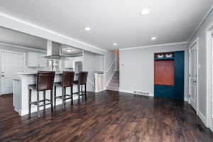 Living room facing kitchen, featuring light countertops, visible vents, dark wood finished floors, white cabinetry, and a breakfast bar area