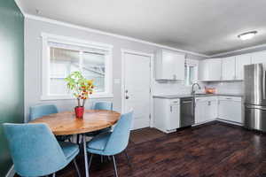 Kitchen featuring a sink, appliances with stainless steel finishes, crown molding, and dark wood-type flooring
