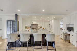 Kitchen with a large island, white cabinetry, light wood-style flooring, and decorative backsplash