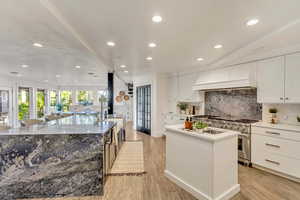 Kitchen with a center island with sink, high end stove, light wood-style floors, custom range hood, and backsplash