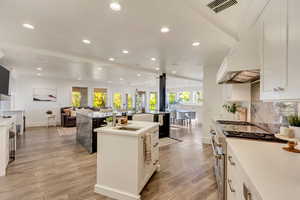 Kitchen with range with two ovens, open floor plan, light wood-style flooring, a kitchen island with sink, and visible vents