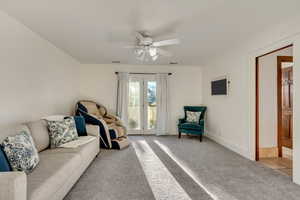 Living room with light carpet, visible vents, and ceiling fan