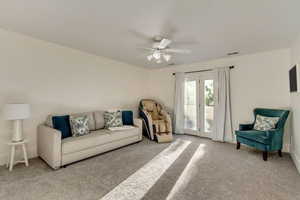 Carpeted living room featuring visible vents and a ceiling fan