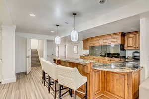 Kitchen with a sink, light wood finished floors, a breakfast bar area, light stone countertops, and decorative backsplash