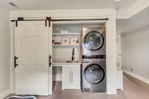 Laundry area featuring visible vents, baseboards, stacked washer / drying machine, a sink, and cabinet space
