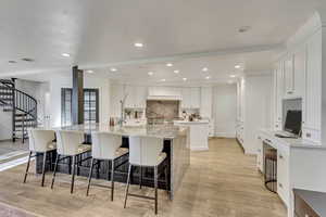 Kitchen featuring white cabinets, a large island with sink, tasteful backsplash, and light wood finished floors