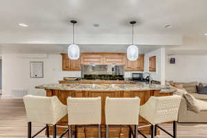 Kitchen featuring visible vents, light stone countertops, a sink, light wood-style floors, and a kitchen breakfast bar