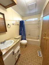 Full bathroom with a textured ceiling, visible vents, toilet, and shower / bathtub combination with curtain
