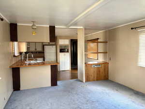 Kitchen featuring a peninsula, a sink, black microwave, carpet floors, and freestanding refrigerator