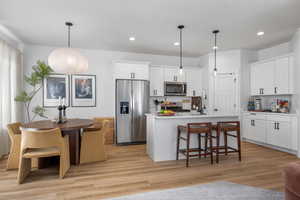 Kitchen with a kitchen breakfast bar, stainless steel appliances, white cabinetry, and light wood-style floors