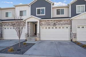 Multi unit property with stone siding, an attached garage, and concrete driveway