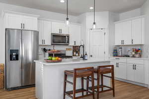 Kitchen with white cabinetry, light countertops, stainless steel appliances, and light wood finished floors