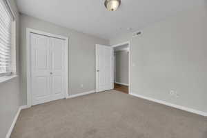 Unfurnished bedroom featuring a closet, carpet floors, visible vents, and baseboards