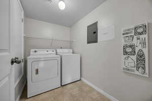 Washroom featuring electric panel, a textured ceiling, laundry area, baseboards, and washer and dryer