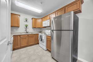 Kitchen with light countertops, a sink, light floors, brown cabinetry, and white appliances