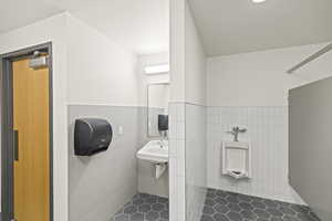 Bathroom featuring tile walls, a wainscoted wall, a sink, and tiled shower