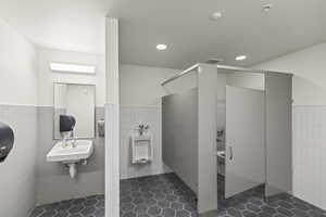 Bathroom featuring tile walls, recessed lighting, a sink, a walk in shower, and wainscoting