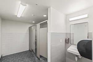 Bathroom featuring a stall shower, a sink, tile walls, and a wainscoted wall